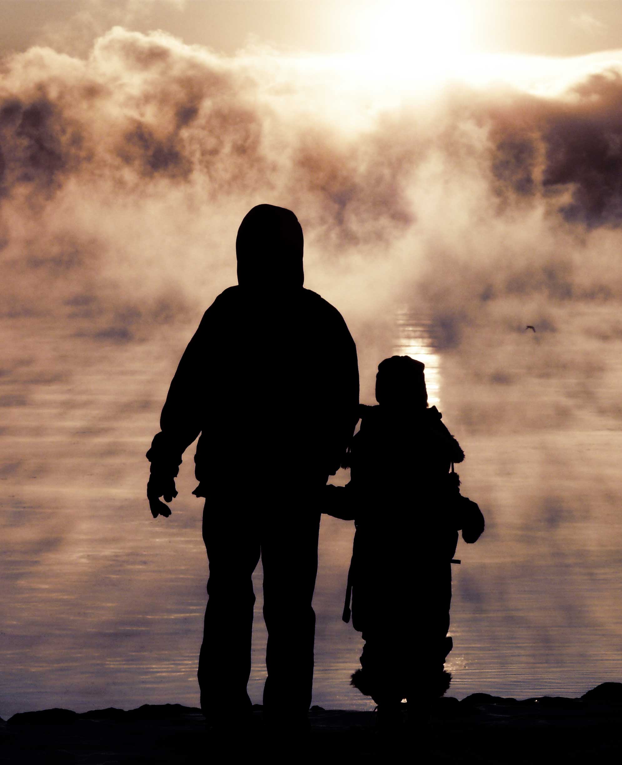 A father holds hands with his daughter as they walk towards the sunset